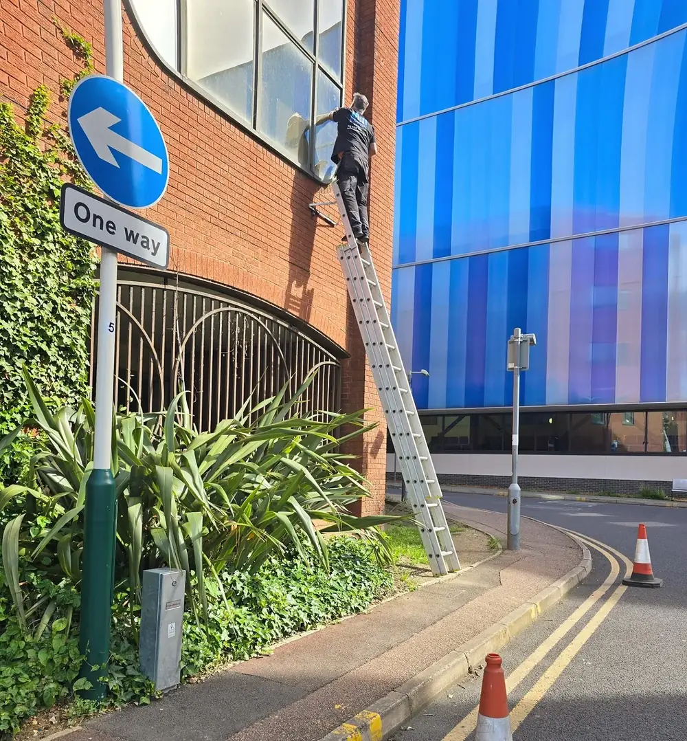 Engineer on a ladder repairing a high-level window on a commercial building